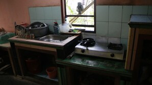 A small kitchen with basic amenities including a sink, a stove, and a window with a view of greenery outside. - Sarjuni Homestay - Hostel (Kokap)
