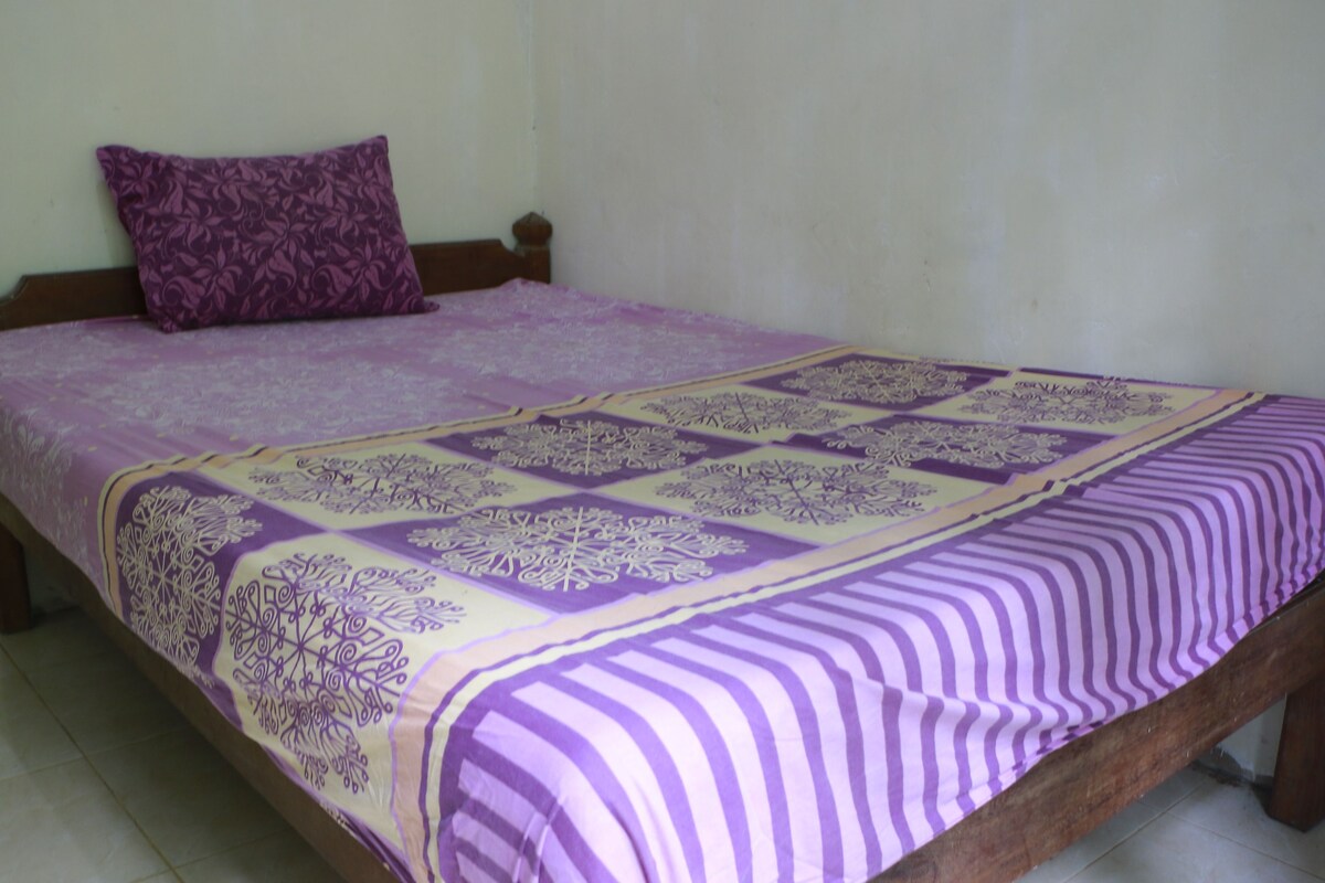 A bed with a purple and white patterned bedspread, a purple pillow, and a wooden headboard.