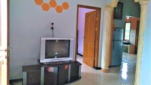 A living room with a television on a stand, a door leading to another room, and a tiled floor. - Villa Trijaya (Batu)