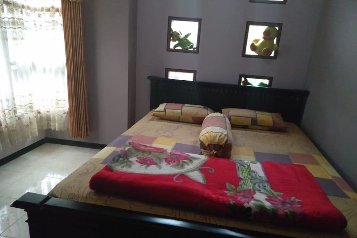 A bed with a floral quilt, a red blanket, and multiple pillows. There are four small windows on the wall.