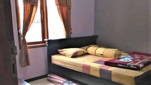A small, single-bed room with a window, curtains, and a bed with a colorful blanket. - Villa Trijaya (Batu)