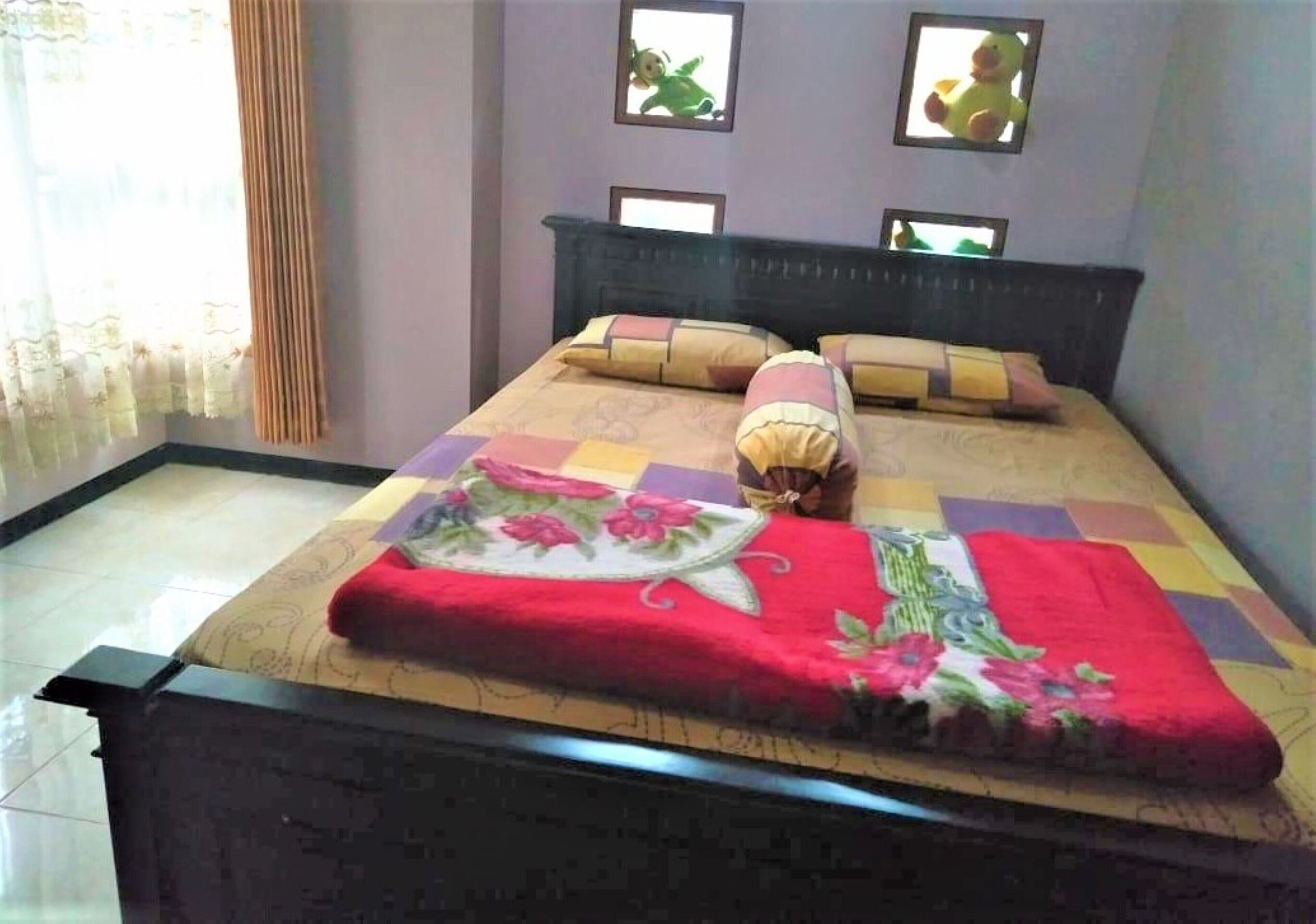 A neatly made bed with a floral bedspread and a red blanket, a dark headboard, and two wall-mounted picture frames.