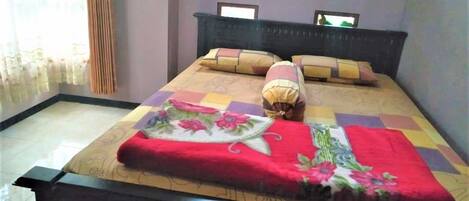 A neatly made bed with a floral bedspread and a red blanket, a dark headboard, and two wall-mounted picture frames.