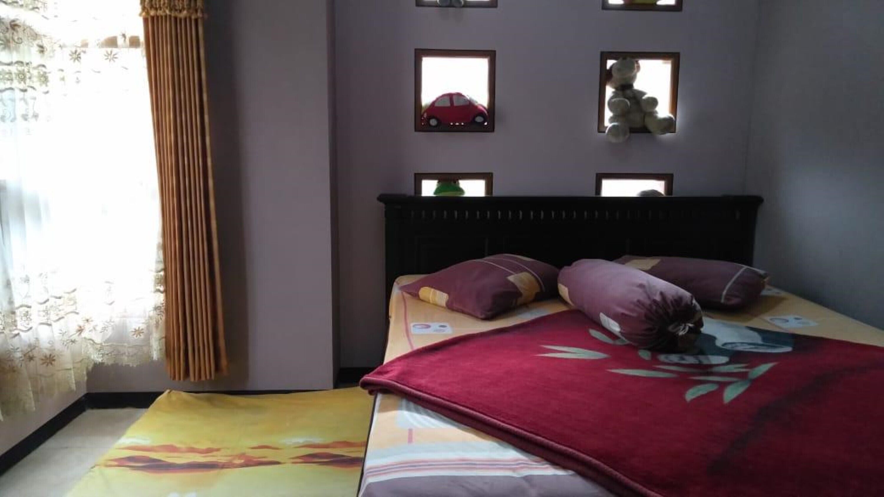 A bedroom with a bed, pillows, a window with curtains, and wall-mounted decorations.