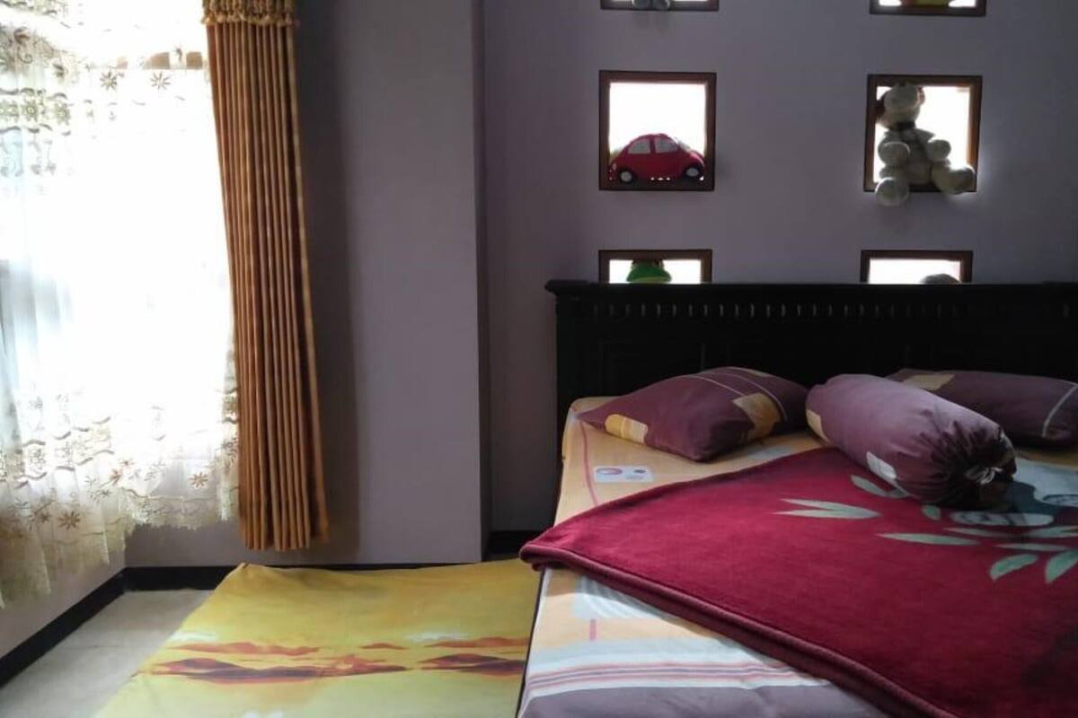 A bedroom with a bed, pillows, a window with curtains, and wall-mounted decorations.