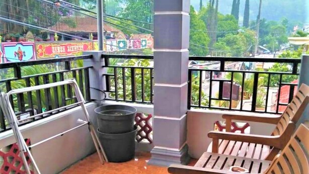 A balcony with a wooden bench, a metal railing, and a trash bin. - Villa Trijaya (Batu)