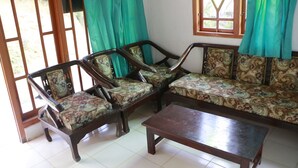 A room with a wooden sofa and chairs, a wooden coffee table, and a window with curtains. - Suparman Homestay - Hostel (Kokap)