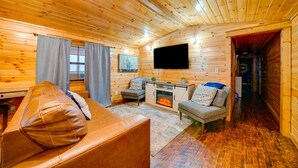 A cozy log cabin interior with a leather sofa, a fireplace, a television, and a small dining area. - Broken Bow Abode w/ Hot Tub < 7 Mi to Lake! (Broken Bow)