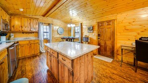 A wooden cabin interior with a kitchen, dining area, and a large wooden door. - Broken Bow Abode w/ Hot Tub < 7 Mi to Lake! (Broken Bow)