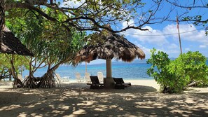 A beach with a thatched umbrella, lounge chairs, and a view of the ocean. - Pili Beach Resort Agmanic (Santa Fe)