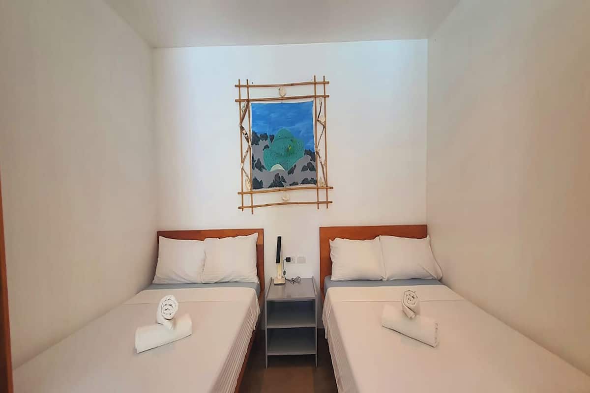 A hotel room with two beds, a small table, a nightstand, and a painting on the wall.