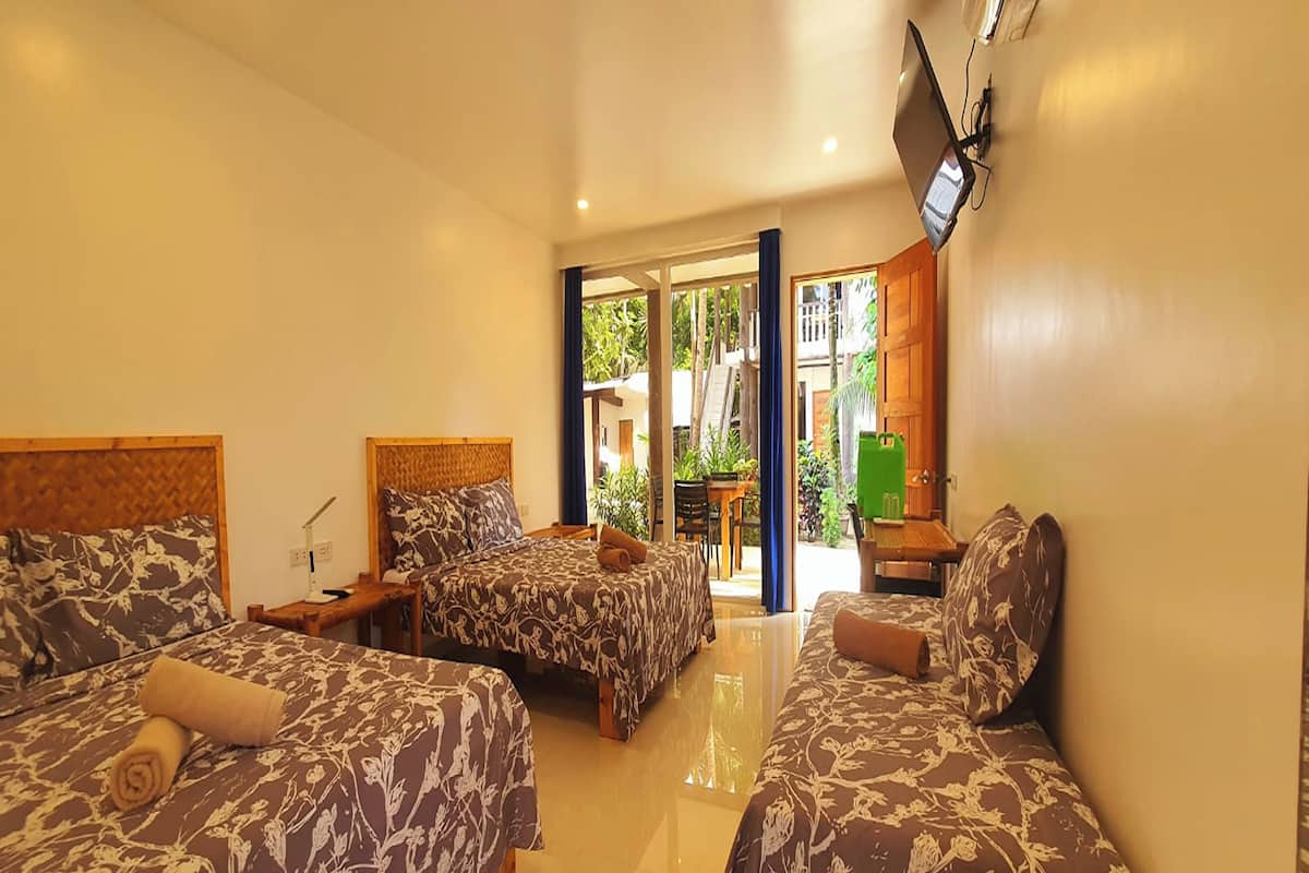 A hotel room with two beds, a TV mounted on the wall, and a view of the outdoor area.