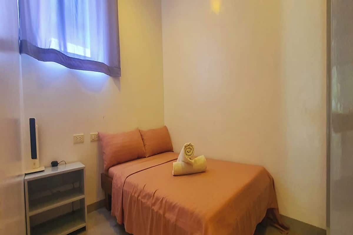 A small, neatly arranged bedroom with a single bed, a bedside table, and a wall-mounted TV.