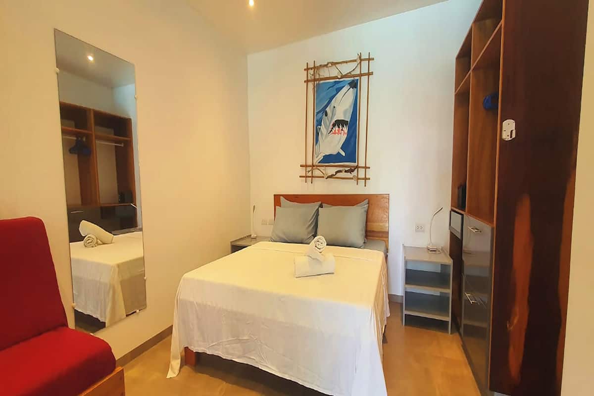 A hotel room with a bed, a red chair, a wardrobe, and a painting on the wall.