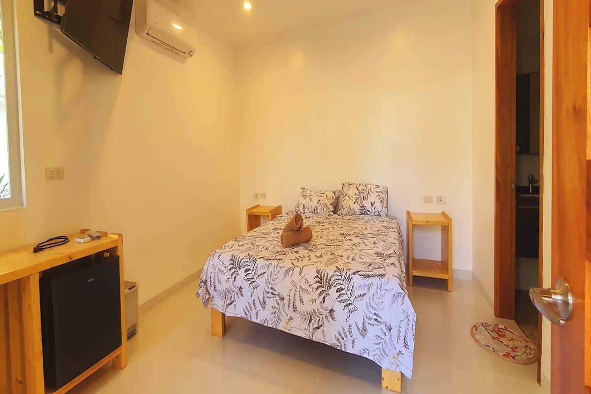 A bedroom with a bed, a TV mounted on the wall, a small desk, and a wardrobe.