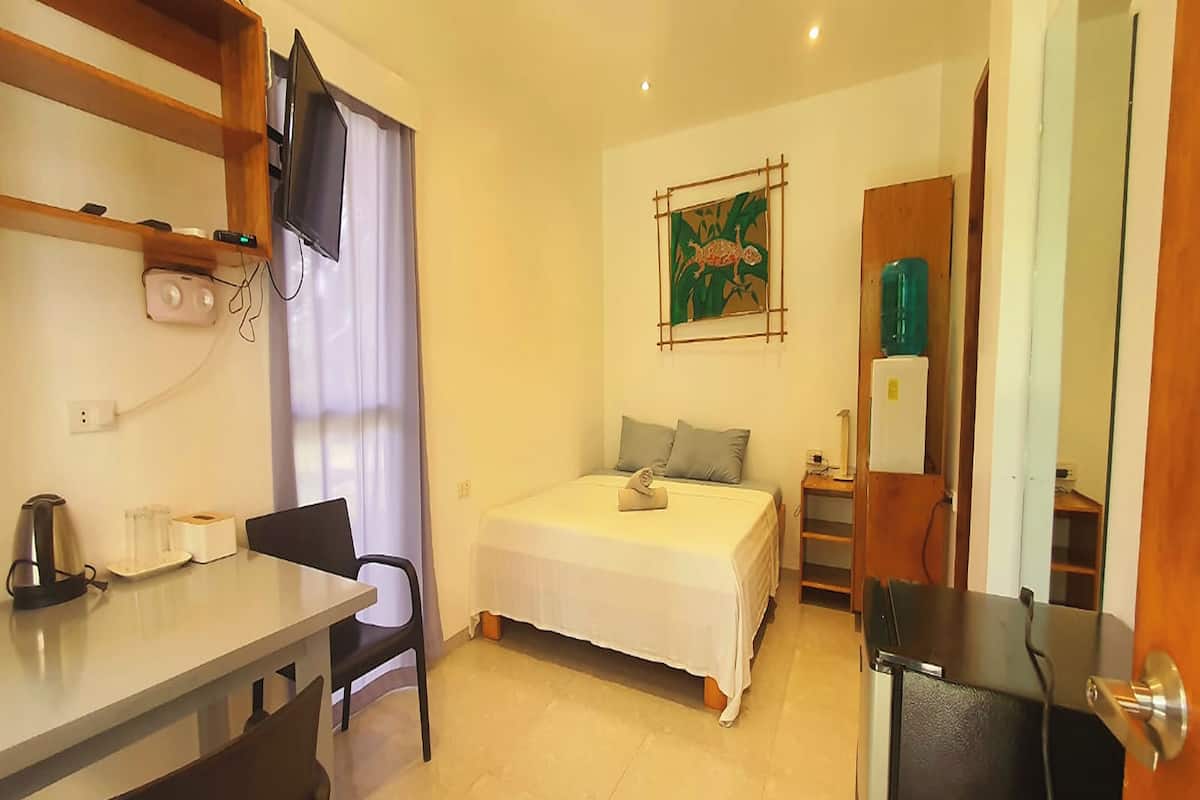 A small, clean room with a bed, a desk, a chair, a TV, and a refrigerator.