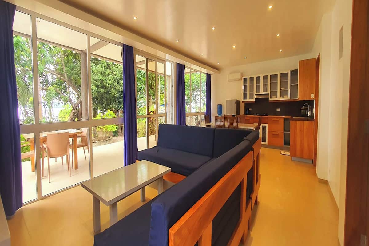 A modern living room with a sofa, a small table, and a view of the outdoors through large windows.