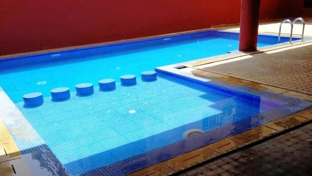 Ein Schwimmbecken mit blau gefliestem Boden und einer roten Wand im Hintergrund.
