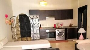 A compact living space with a sofa, a coffee table with magazines, a washing machine, and a kitchenette with dark cabinets and a microwave. - Residence La Kasbah de Marrakech 4640 (Marrakech)