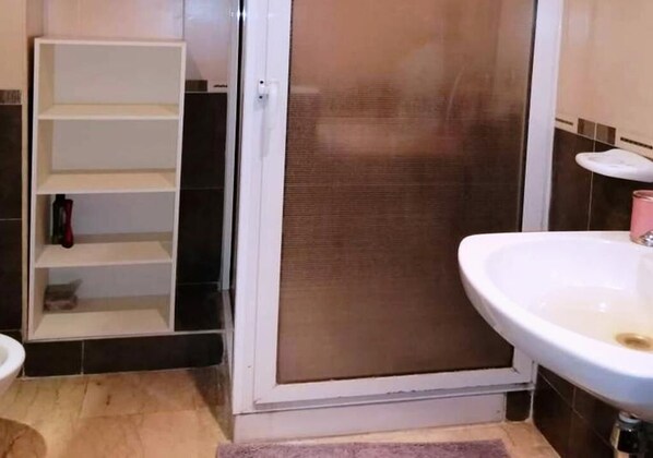A bathroom with a white sink, a shower enclosure, and a white shelf unit.