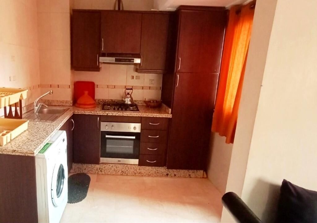 Cocina compacta con armarios de madera oscura, horno empotrado, estufa a gas y lavadora.