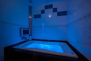 A bathroom with a bathtub, a mirror, and a wall-mounted control panel.