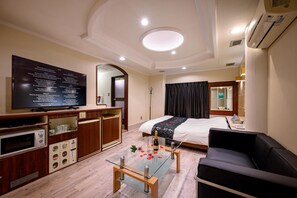 A hotel room with a bed, a TV, a desk, a glass coffee table, and a sofa.