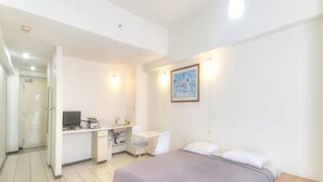 Une chambre d’hôtel de taille réduite, comprenant un lit, un petit bureau, une chaise et une kitchenette.