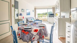 Ruokailutila, jossa on neljälle katettu ruokapöytä, sohva ja taustalla televisio.