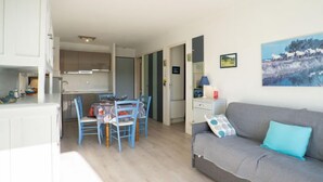 Kompakti oleskelutila, jossa on pieni keittiö, ruokailualue ja sohva, jossa on tyyny.