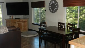 A dining area with a wooden table and chairs, a television mounted on the wall, and a large clock. - Anderson Island's most peaceful home (Anderson Island)