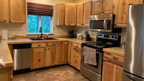 A modern kitchen with wooden cabinets, stainless steel appliances, a granite countertop, and a window with a view of trees. - Anderson Island's most peaceful home (Anderson Island)