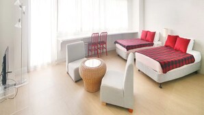 A bright, modern room with two beds, a sofa, a chair, and a lamp. - Pia Resort Hotel Corner Studio Room 3 (Tamuning)