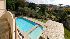 A swimming pool with stone tiles, surrounded by greenery and buildings in the background. - Pia Resort Hotel Corner Studio Room 3 (Tamuning)