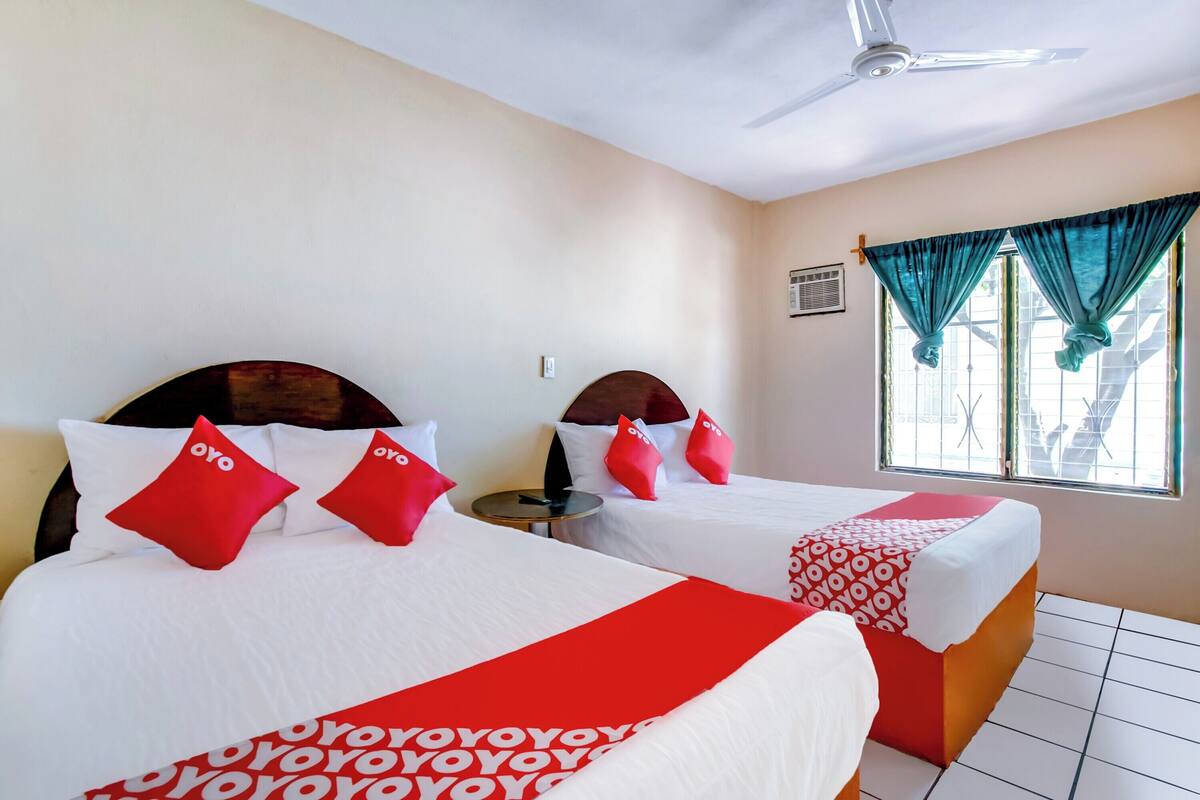 A hotel room with two beds, each with red and white bedding, a ceiling fan, and a window with curtains.