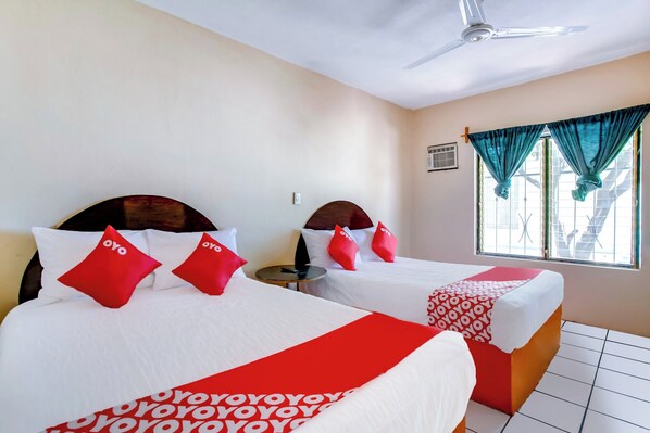 Habitación de hotel con dos camas, cada una con ropa de cama roja y blanca, un ventilador de techo y una ventana con cortinas.