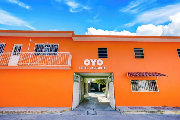 Un edificio anaranjado brillante con el letrero "OYO HOTEL MARGARITAS" y una entrada protegida por una reja.