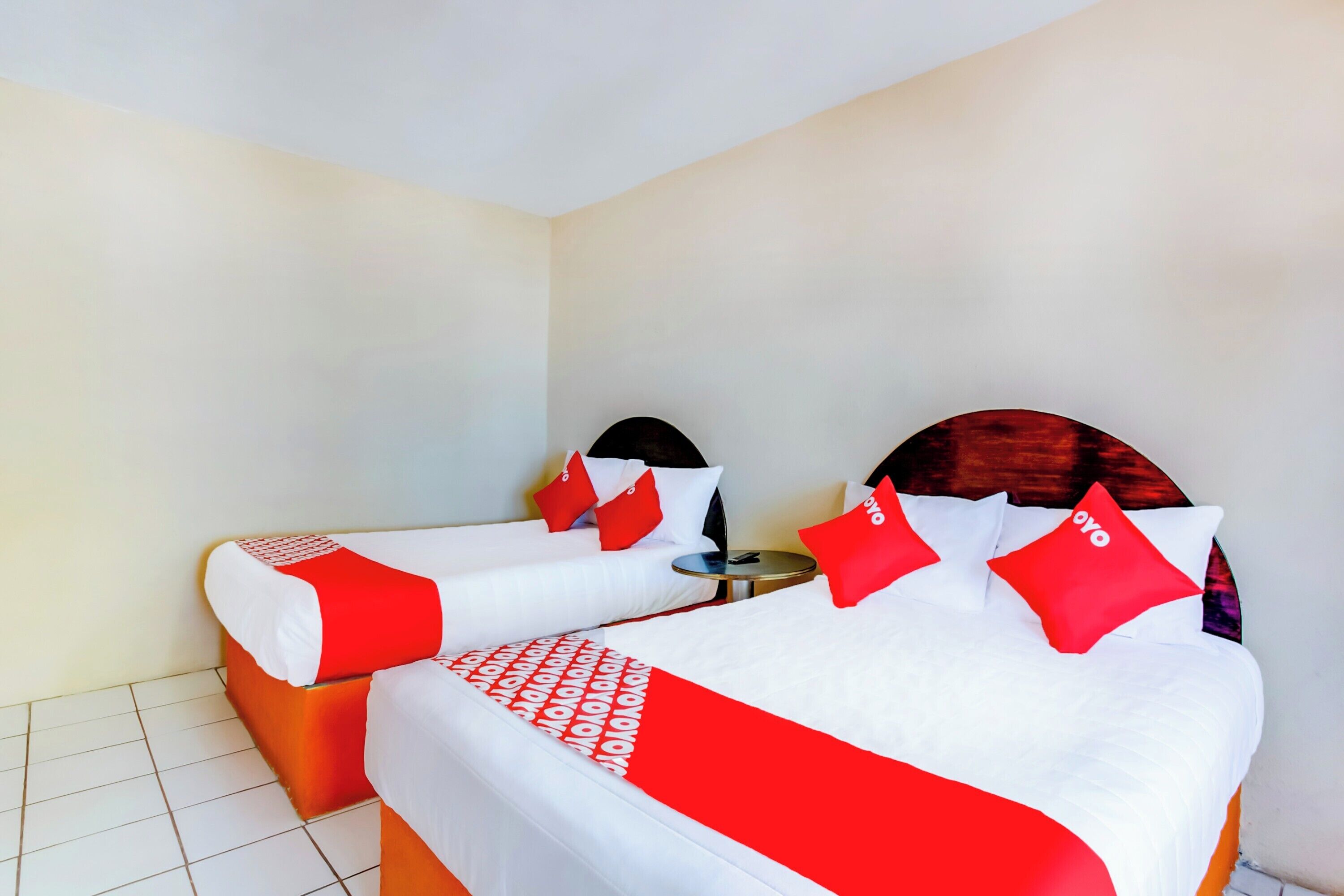 Una habitación de hotel con dos camas, cada una con ropa de cama roja y blanca, y una mesita redonda entre ellas.