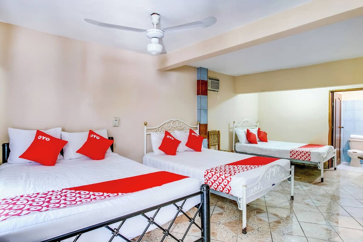 A hotel room with three beds, each with white bedding and red pillows, a ceiling fan, and a tiled floor.