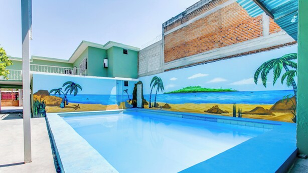 Une piscine ornée d’une fresque représentant une scène de plage, avec des palmiers et un coucher de soleil sur l’océan.