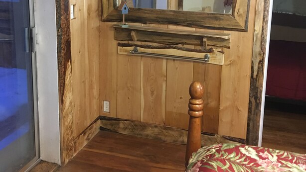 A bedroom with wooden walls, a large mirror, a wooden bed frame, and a floral bedspread. - great for kids - pets welcome - self check in - downtown - kitchen and laundry (Idaho Falls)