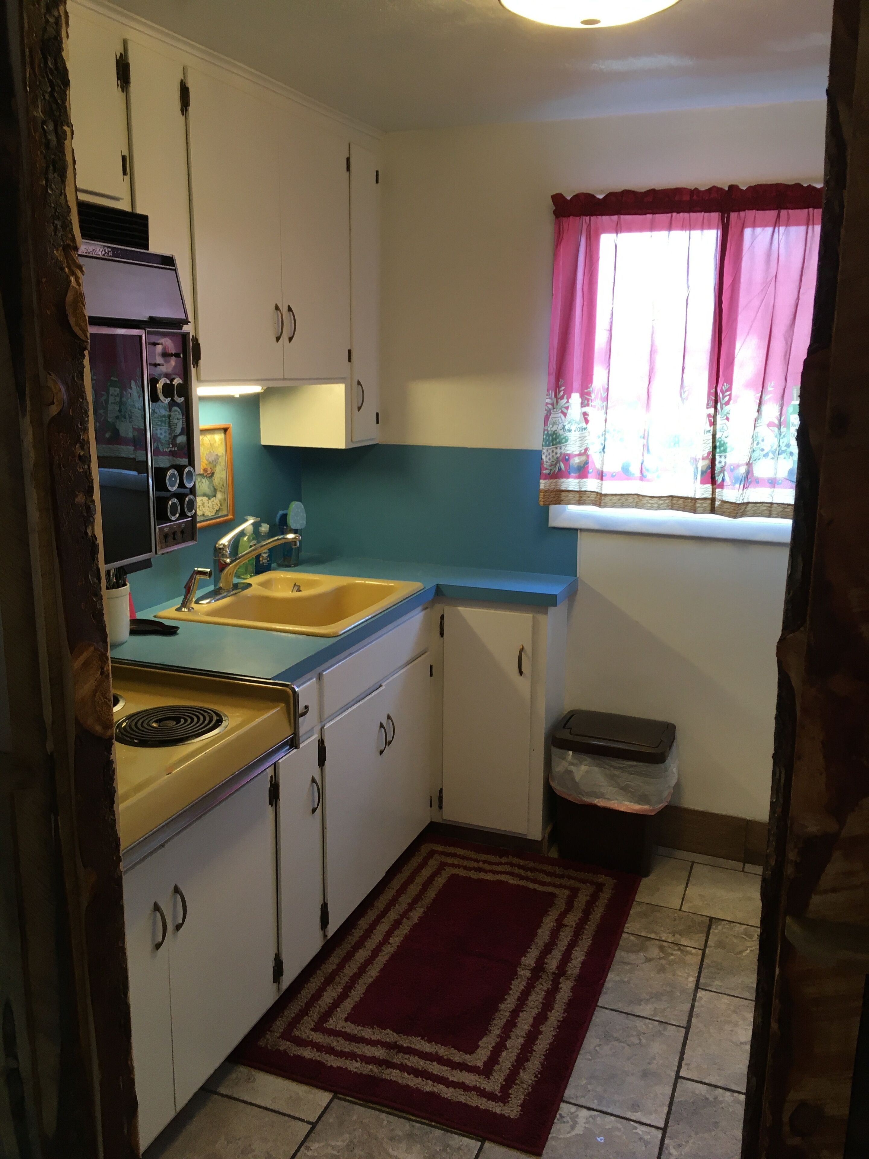 A compact kitchen with white cabinets, a blue countertop, a sink, and a stove.