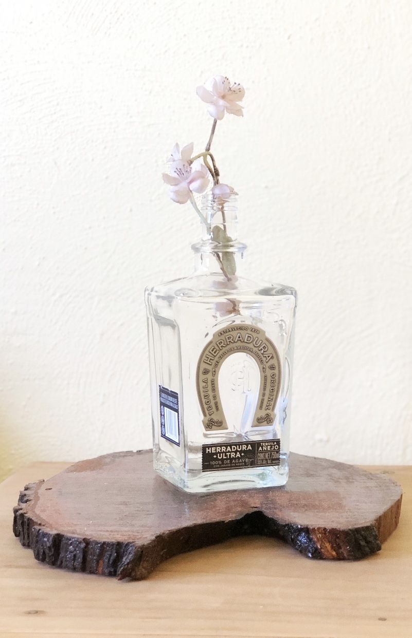 Una botella de vidrio transparente con etiqueta, sobre un posavasos de madera.