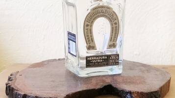 Una botella de vidrio transparente con etiqueta, sobre un posavasos de madera.