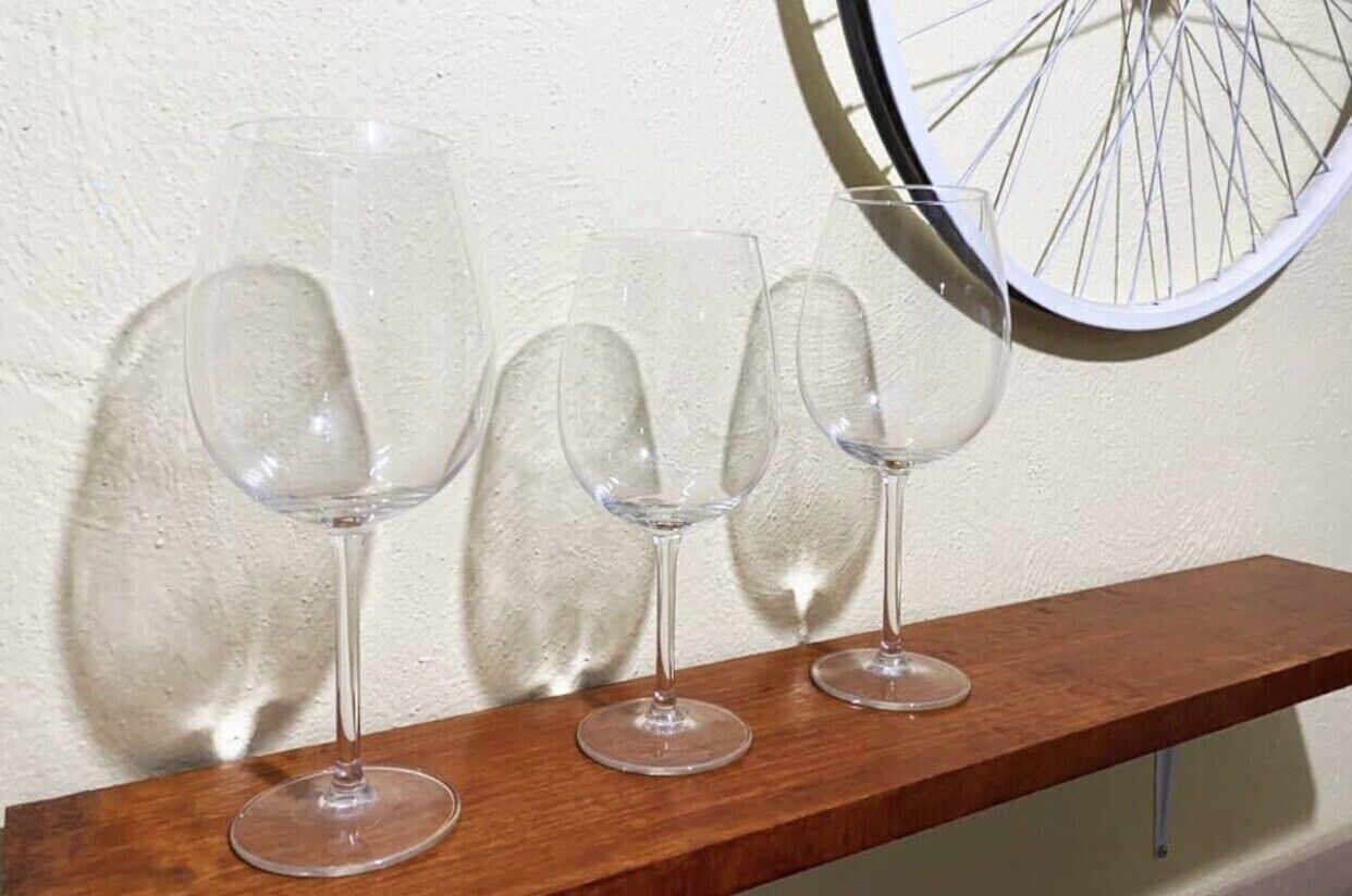 Tres copas de vino vacías sobre un estante de madera frente a una pared con textura.