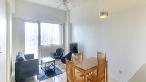 A modern living room with a dining area, large windows, and a ceiling fan. - Pia Resort Hotel Standard 2 Bedroom 2 (Tamuning)