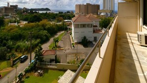 A residential area with a view of a white building with a tiled roof, surrounded by greenery and a road. - Pia Resort Hotel Standard 2 Bedroom 2 (Tamuning)