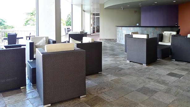 A spacious outdoor area with wicker furniture and a stone-tiled floor, featuring a seating area and a reception desk. - Pia Resort Hotel Standard Studio 2 (Tamuning)