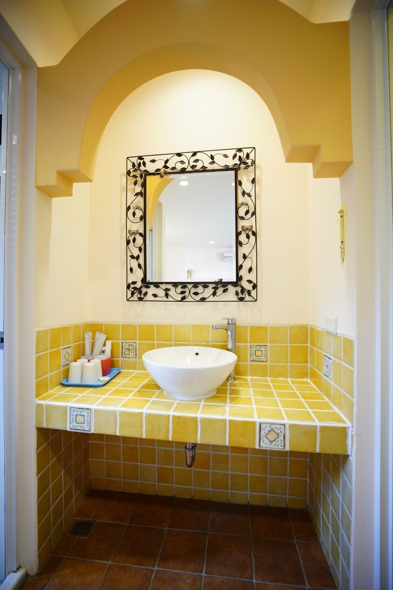 Un baño con un lavamanos blanco, baldosas amarillas y un espejo con marco decorativo.