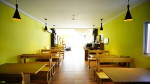 A restaurant with wooden benches and tables, bright yellow walls, and black pendant lights. - Kenting Wonderful Hotel (Hengchun)